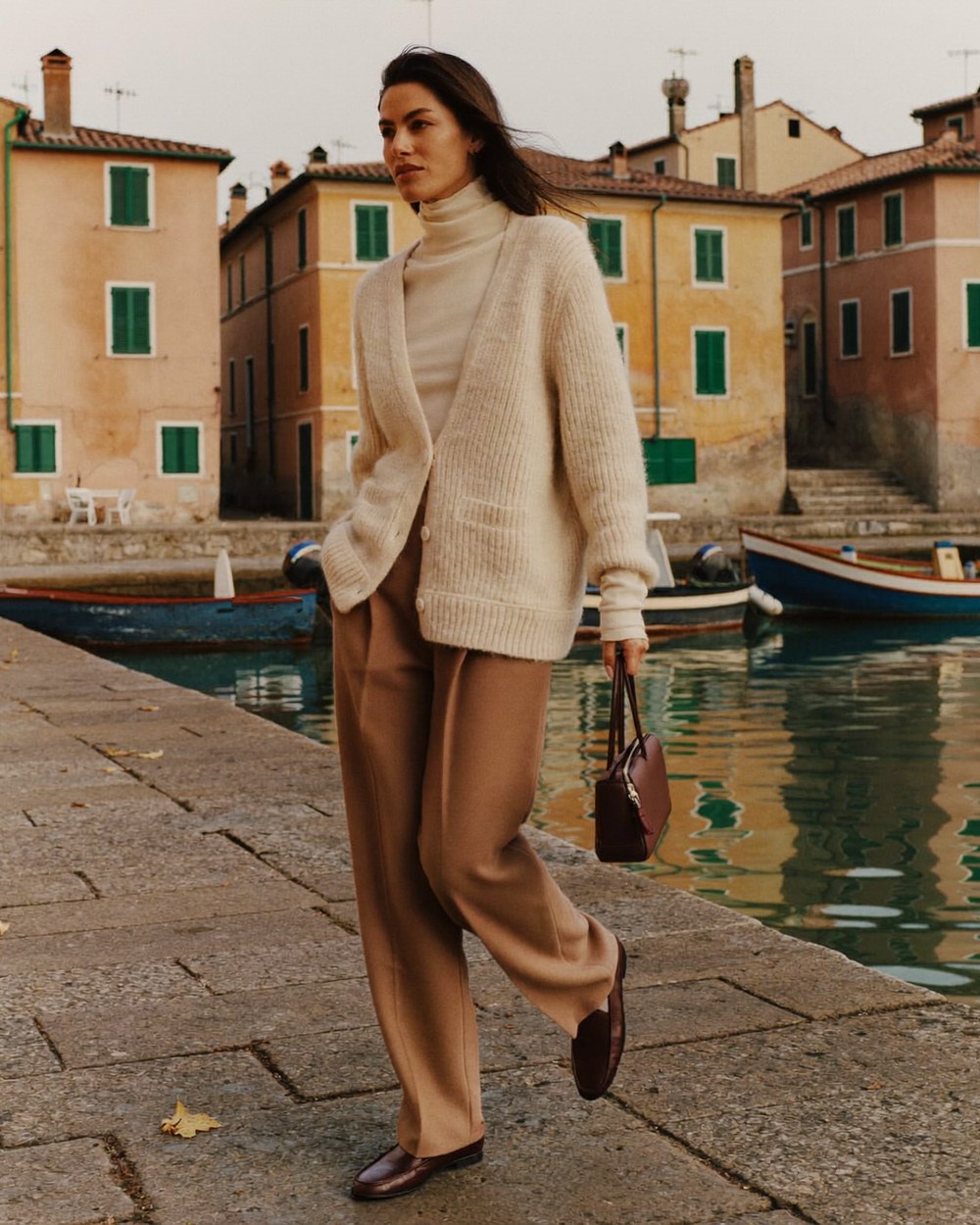 Donna con cardigan in maglia che passeggia in un porto italiano in autunno